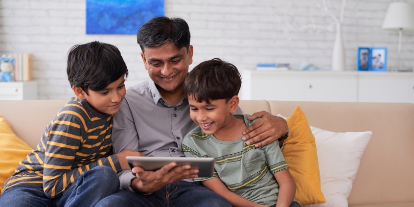 A family smiling together, looking at a tablet.