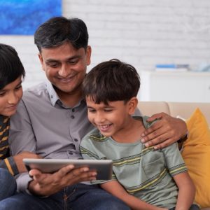 A family sit together, looking and smiling at a digital tablet.