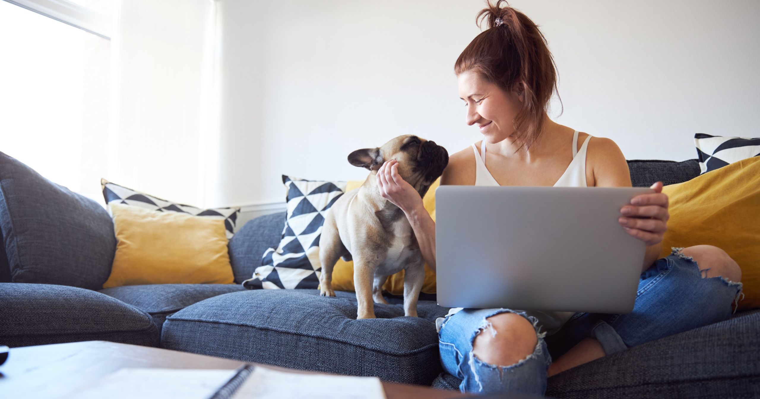 Woman smiling at her dog with her laptop on her lap.